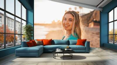 Portrait of one happy beautiful woman on the sand of the beach enjoying and having fun at the sunset of the day. Looking at the camera smiling.. Wall mural