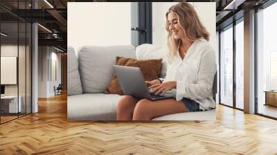 Portrait of one young attractive blonde woman using laptop pc computer on couch relaxing surfing the net at home. Working online concept lifestyle. Wall mural