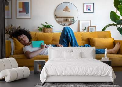 Tired African American woman sleeping on yellow couch after reading a book Female relaxing at home. Wall mural