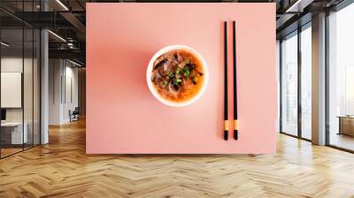 Top view of a bowl with oriental soup with chopsticks on pink background. Food. Wall mural