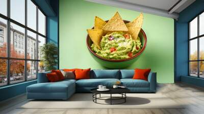 Top view of avocado guacamole dip with salted tortilla chips in bowl on green background Wall mural