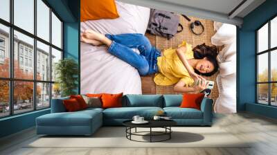 Top view of teen asian girl relaxing at home after class, lying on bedroom floor using phone. Wall mural