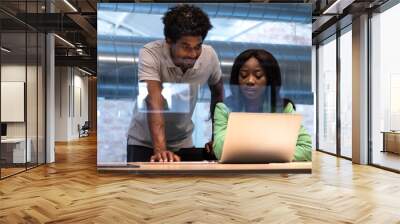 Two african american coworkers analyse reports together at the office using laptop. Wall mural