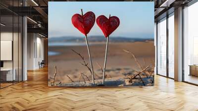 Two heart shaped cutouts in vibrant red color are attached to the tops of sticks creating a lovely and romantic picture against the backdrop of a sandy beach with an unoccupied area for additional im Wall mural