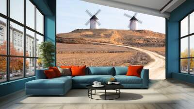 two windmills in the countryside with dirt road and straw blue sky, donquijote fields in castilla la mancha in spain europe Wall mural