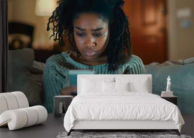 Woman on couch watching videos on smartphone with worried expression in living room. African American woman and cellphone with network signal, social media, or communication connection Wall mural