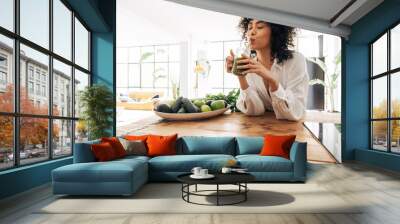 Young african american woman drinking green juice with reusable bamboo straw in loft apartment Wall mural