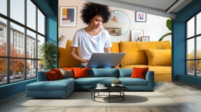 Young African american woman sitting on the couch using laptop working at home. Copy space. Wall mural