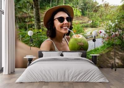 Young female tourist taking selfie with phone while drinking coconut water in Tegalalang rice terrace, Bali. Copy space. Wall mural