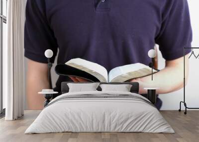 Young man reading a small Bible wearing a navy shirt. Wall mural