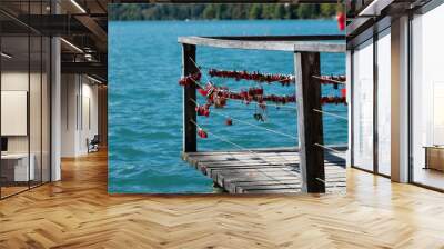 Love locks of a wooden pier facing a lake in autumn: a promise made. In the background we see the blue waters of lake Bled in Slovenia and a red buoy, man shaped. It is a sunny day. Wall mural