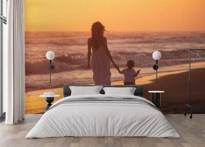 A mom with her child walk on the beach of a beautiful shore at the sunset light Wall mural