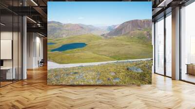 Top view from grassy stone pass to two blue lake among green hills in bright sun. Sunlit valley between multicolor mountains of many pastel colors in sunny day. Mountain range silhouette far away. Wall mural