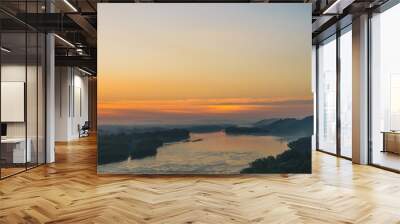 View from high shore on river. Riverbank with forest under thick fog. Gold dawn reflected in water. Orange glow in picturesque predawn sky. Mystical morning atmospheric landscape of majestic nature. Wall mural