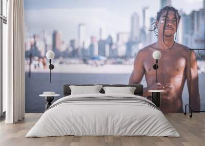 17-year-old Afro-descendant teenager with braids in his hair and no shirt, various facial expressions, city of Balneário Camboriu in the background is blurred Wall mural