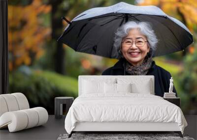 A smiling asian senior woman holding a umbrella in a park Wall mural