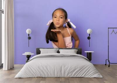 Beautiful little girl wearing swimwear sending air kiss isolated over purple background. Wall mural