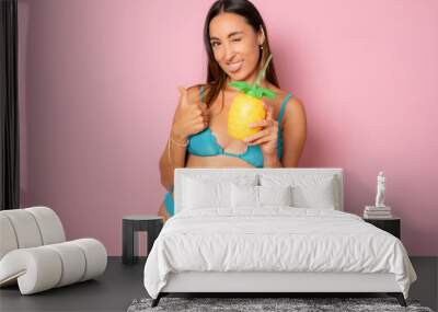 Beautiful smiling woman in bikini drinking juice isolated over pink background. Wall mural