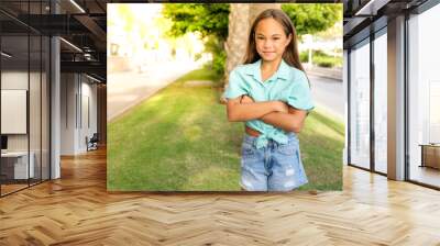 Close up portrait of a smiling child girl in spring park on sunny warm day with arms folded. Wall mural