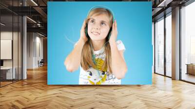 Cute adorable girl wearing headphones and enjoying music over blue background. Wall mural