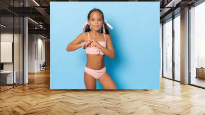 Cute little girl in swimwear making heart figure gesture isolated over blue background. Wall mural