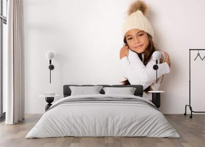 Cute smiling girl wearing winter hat hugging herself on white background Wall mural