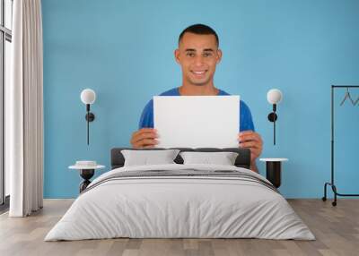 Handsome young man is holding a sheet of paper on blue background Wall mural