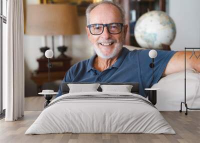 Head shot portrait close up smiling older retired man sitting on couch at home, happy friendly grandfather looking at camera, mature grey haired male posing for photo on sofa, feeling positive Wall mural