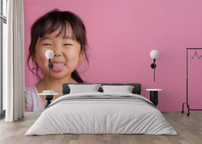 headshot portrait of playful female child tilted her head and shows her tongue standing over a pink isolated background Wall mural