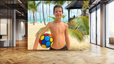 Portrait of a cute European teen boys wearing swimming shorts. The boy standing on the beach holding a ball. Wall mural