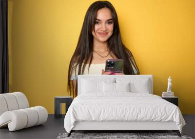 Portrait of a smiling casual woman holding smartphone over yellow background Wall mural