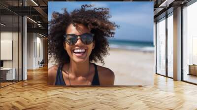 Portrait of young african american woman with curly hair at beach. Smiling black woman walking at the seaside while looking at camera. Happy carefree girl at sea. Wall mural