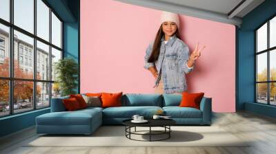 Pretty brunette kid girl wearing white winter hat over pink background Doing peace symbol with fingers, smiling cheerful showing victory Wall mural