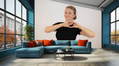 Smiling young girl in black dress showing heart with two hands, love sign. Isolated over white background. Wall mural