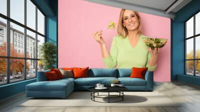 Young woman eating a healthy salad isolated over pink background. Wall mural