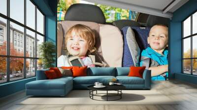 two little kids sitting on back seat in child safety seats Wall mural