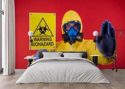 A man in a protective chemical mask and a protective yellow suit with a banner in his hand with the words biohazard shows a stop sign. Biohazard concept Wall mural