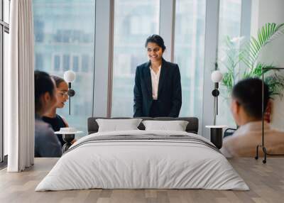 An Asian Indian businesswoman is having a conversation with her colleagues in a conference room. She's smiling elegantly.  She's wearing a black blazer and white blouse with a black skirt. Wall mural