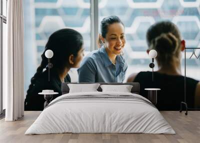 Image of a young Asian Chinese woman manager in their office chatting with her team. She is smiling as she listens to her colleague discussing something about their new project. Wall mural