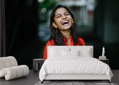 Portrait of attractive and young Indian woman laughing in an orange ethnic dress during the day Wall mural