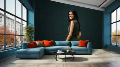 Portrait of cheerful and smiling young Indian lady in a grey jumpsuit against a dark wall Wall mural