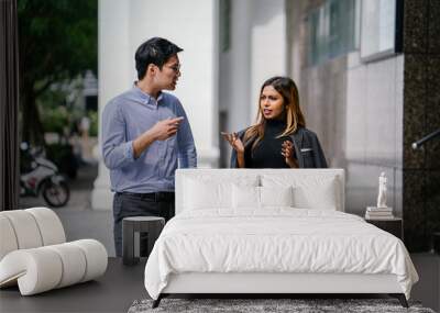 Two diverse Asian businesspeople (colleagues meeting for lunch) walking in the city. One is a Korean man, the other is a Malay woman. They are both seriously speaking as they chat. Wall mural