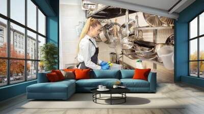 Young woman washing dishes using sponge in restaurant sink at end of working day  Wall mural