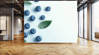 A handful of blueberries scattered on a white background. The deep blue color contrasts against the clean surface, with a few leaves for added realism. Wall mural