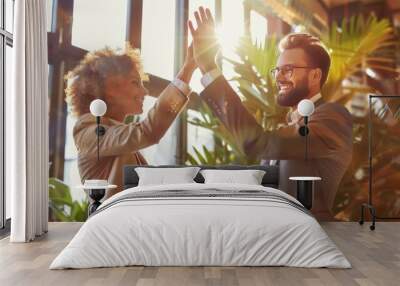 Successful business people giving each other a high five in a meeting. Two young business professionals celebrating teamwork in an office. Wall mural