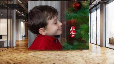 Close-up happy little boy in a red jacket looking with curiosity at a Christmas tree toy  Wall mural