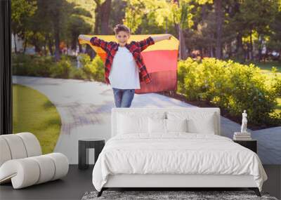 Guy of 9 years old riding skateboard on sunny road in the evening in the city park. Holding fluttering flag of Germany. Happy German day. German language, European education Wall mural