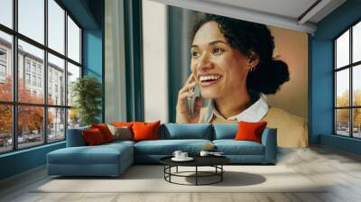 Happy young woman talking on mobile phone at home standing near window and looks away Wall mural