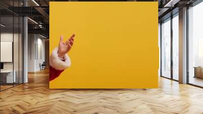 Cheerful Santa Claus, dressed in a traditional red suit, stands against a bright yellow background, gesturing with his hand toward the copy space. Merry Christmas and Happy New Year holiday. Wall mural