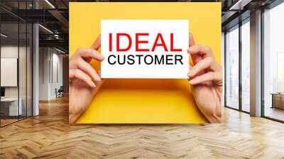 Female hands hold card paper with text IDEAL CUSTOMER on a yellow background. Business and finance concept Wall mural